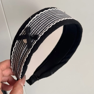 Close-up of black padded headband featuring white lace edges and a satin bow detail