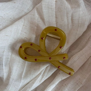 Close-up of olive green bow hair claw clip with red polka dots and metal spring detail