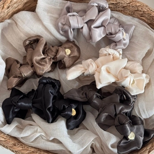Elegant satin bow hair claw clips in various colors with golden logo charms in a basket