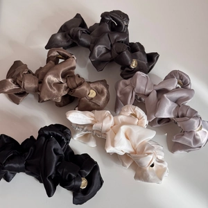 Detailed close-up of large satin bow hair claws with elegant metallic emblem details