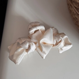 Detail of a large cream satin bow hair claw clip featuring soft textured fabric finish