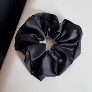 Dettaglio di un grande elastico in raso nero con morbide pieghe e ciondolo a cuore