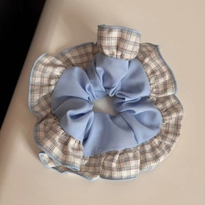 Detail eines hellblauen Haargummis mit Karomuster, Chiffon-Textur und Rüschendesign