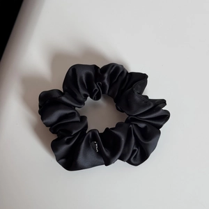 Dettaglio dello scrunchie in raso nero con un delicato ciondolo a cuore in argento