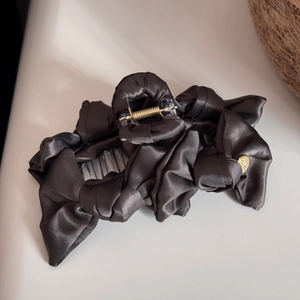 Close-up of a large dark grey satin hair claw clip with elegant knot detailing