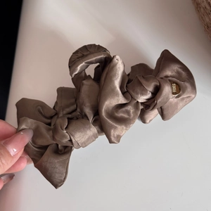 Close-up of champagne satin bow hair claw clip with golden metal logo buckle detail