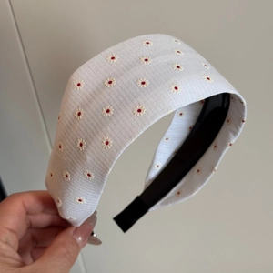 Detailansicht eines weißen Stoffstirnbandes mit bestickten Gänseblümchen und roten Mitten