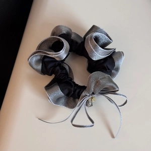 Detail of ruffled scrunchie with silver accents, bow tie, and metallic charm pendant