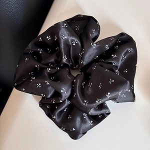 Gros plan sur chouchou en satin noir à fleurs avec texture soyeuse et motifs blancs