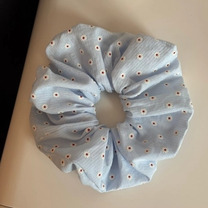 Detail eines hellblauen Scrunchie aus Rippstoff mit gestickten weißen Gänseblümchen