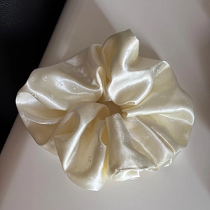 Gros plan sur un chouchou en satin crème avec motif floral élégant et texture soyeuse