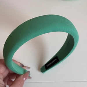 Detail of emerald green sponge headband featuring a woven handmade label and fabric texture