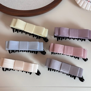 Detailed close-up of six pastel satin bow banana clips in creamy yellow and violet