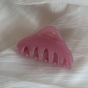 Détail d'une pince à cheveux triangulaire rose translucide sur tissu blanc texturé
