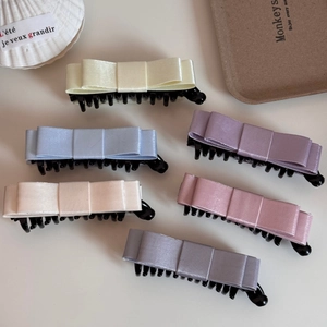 Close-up of six satin bow banana hair clips in elegant Morandi colors on a white surface