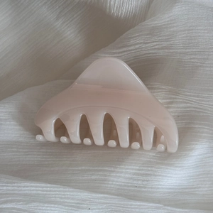 Détail d'une pince à cheveux triangulaire crème sur fond de tissu blanc doux et élégant