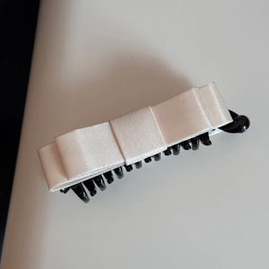 Macro shot of the layered white satin bow and black plastic comb teeth on the banana hair clip