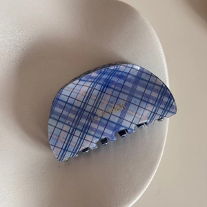 Macro detail of blue and purple plaid hair claw clip with golden logo in a beige ceramic dish