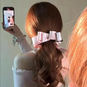 Detailed view of a pink satin polka dot bow hair clip on a low ponytail with ribbons