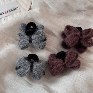 Détail de pinces à cheveux à nœuds tricotés gris et rouge foncé sur tissu beige doux