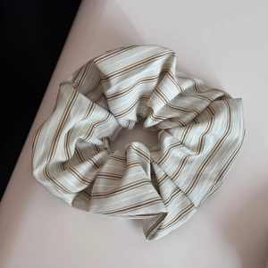 Détail d'un grand chouchou en tissu rayé beige et marron avec une texture plissée douce