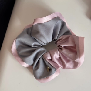 Close-up of dual-tone grey and pink satin hair scrunchie with a gold metal charm