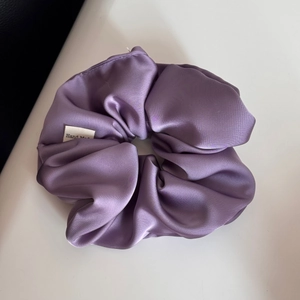 Detailed view of a purple satin hair scrunchie featuring a handmade woven label tag