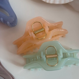 Vue détaillée de pinces à cheveux en résine pastel avec ressorts dorés sur plateau