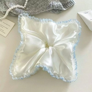 Détail d'un chouchou en satin blanc avec bordure en dentelle bleue et fini soyeux