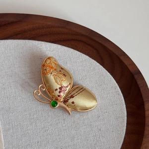 Detailansicht der Schmetterlingsbrosche mit goldener Seidenstickerei und grünem Edelstein