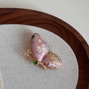 Detail einer Schmetterlingsbrosche aus rosa Seide mit Goldstickerei und grünem Stein