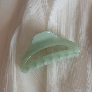 Détail d'une pince à cheveux évidée vert clair sur fond de tissu blanc à texture plissée