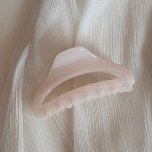 Détail d'une pince à cheveux crème minimaliste avec design ajouré sur tissu plissé blanc