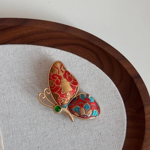 Detailaufnahme der Schmetterlingsbrosche aus Song-Brokat mit grünem Edelstein und Goldrahmen