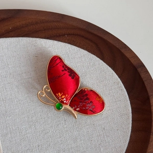 Makroaufnahme der Schmetterlingsbrosche aus roter Jacquard-Seide mit Goldrahmen