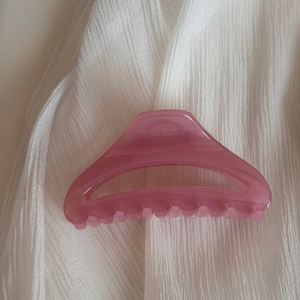 Vue détaillée d'une pince à cheveux rose translucide sur fond de tissu blanc texturé
