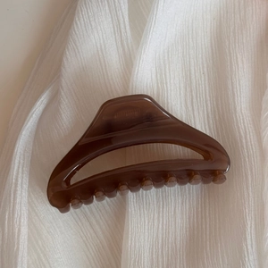 Détail de la pince à cheveux évidée marron café avec texture de résine sur tissu blanc