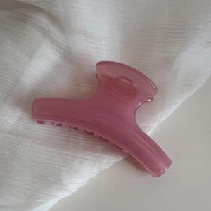 Detail view of pink translucent matte hair claw clip on white textured fabric background
