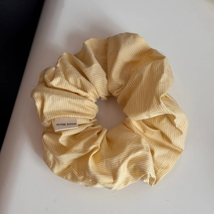 Detail eines handgefertigten gelb-grau gestreiften Satin-Haargummis auf weißem Grund