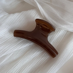 Close-up of a polished amber brown hair claw clip on a white textured fabric background