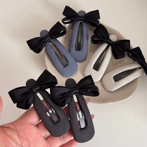 Trois barrettes à cheveux élégantes avec nœuds en tissu noir, gris et beige sur une assiette