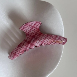 Close-up of pink checkered hair claw clip with golden lettering in a ceramic dish