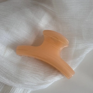 Close-up of a large orange-pink hair claw clip with a glossy translucent finish on white fabric