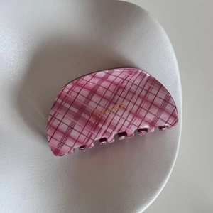 Detailed view of a pink checkered hair claw clip with golden logo in a white ceramic dish
