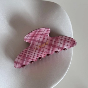 Close-up of pink checkered hair claw clip with gold logo detail on white ceramic plate