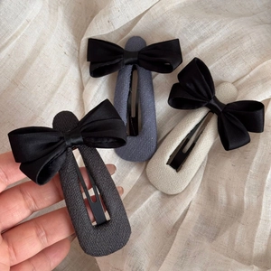 Vue détaillée de trois barrettes à nœud en noir, gris et crème avec texture de satin