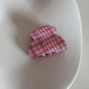 Detail of pink checkered shark hair clip with gold logo on a white textured ceramic tray