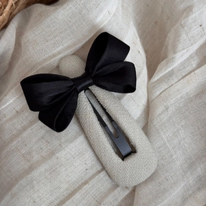 Gros plan détaillé d'une pince à cheveux avec nœud en satin noir et texture en lin beige