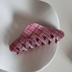 Top view of pink checkered hair claw clip with golden brand logo on a white tray