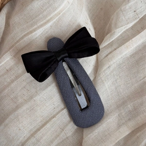 Détail d'une pince BB vintage en tissu gris avec un nœud en satin noir élégant